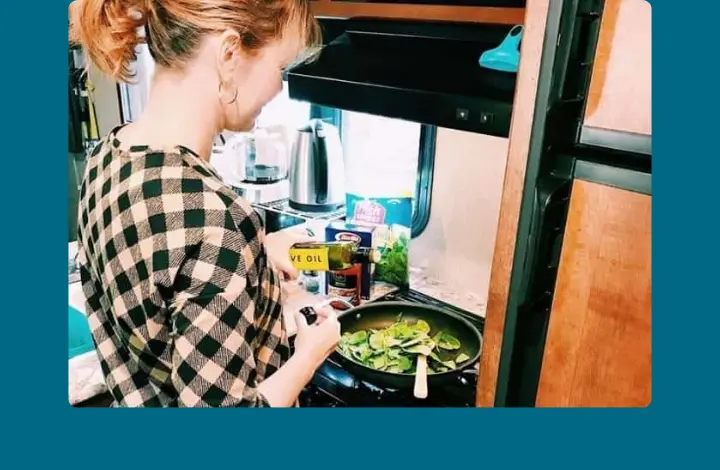 Woman standing at stovetop inside RV cooking spinach in a skillet