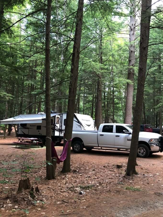 White towing truck and travel trailer parked at campsite with hammock installed between trees.
