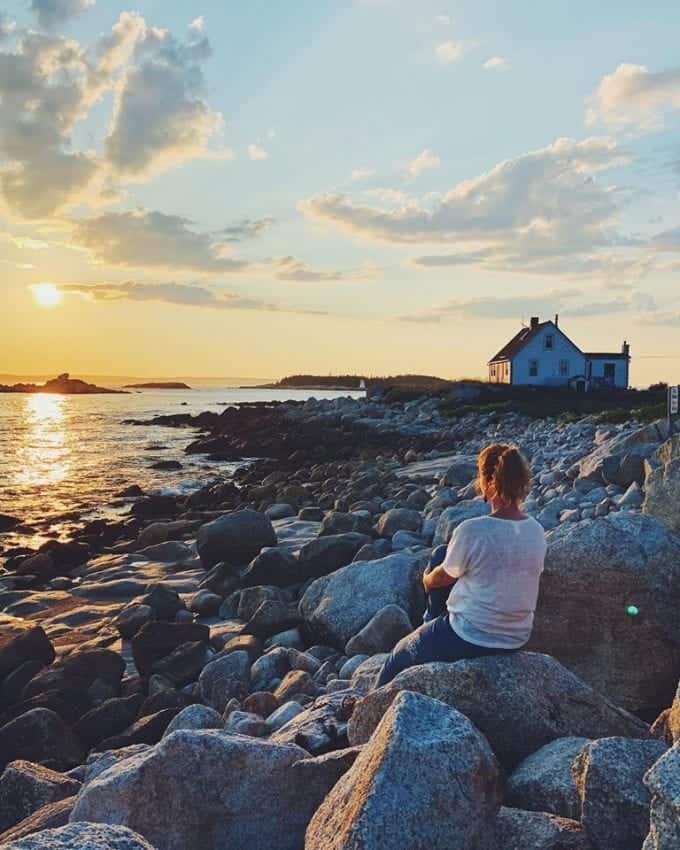 Woman sitting on large boulder near the sea watching the sunset.