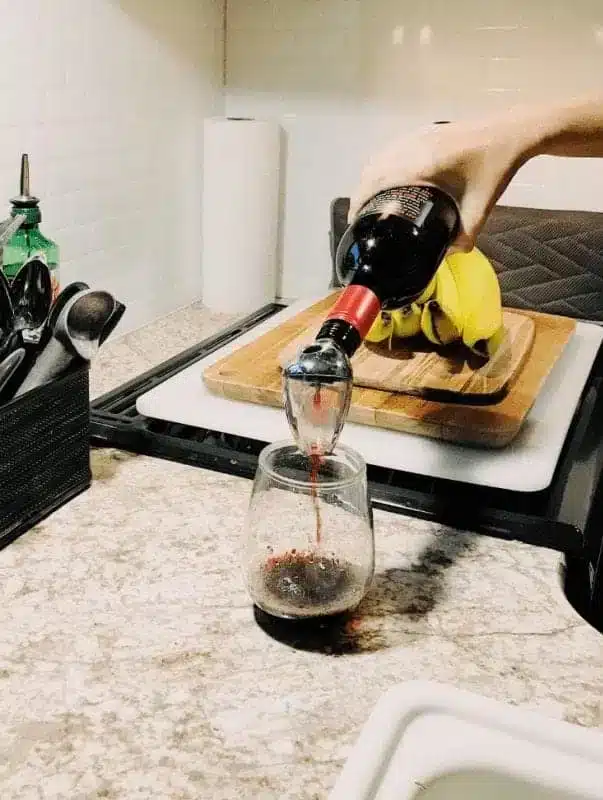 Someone pouring red wine into glass inside RV kitchen.