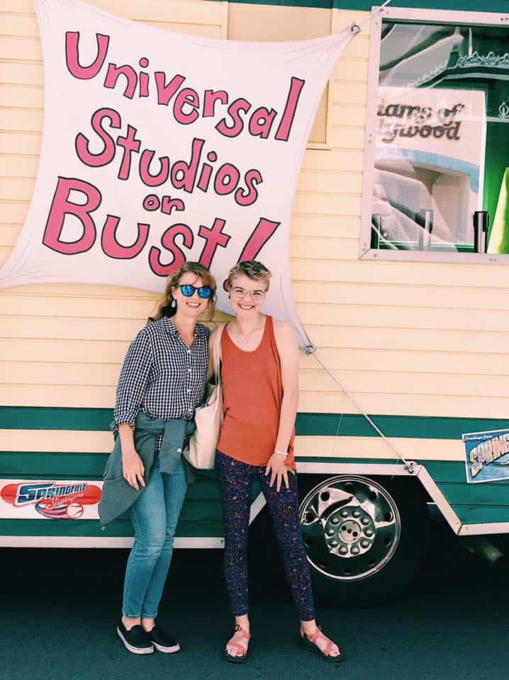 Mother and daughter in front of RV rental with sign that reads 'universal studios or bust'