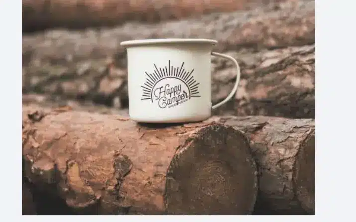 Camping mug with text 'happy camper' set on firewood.