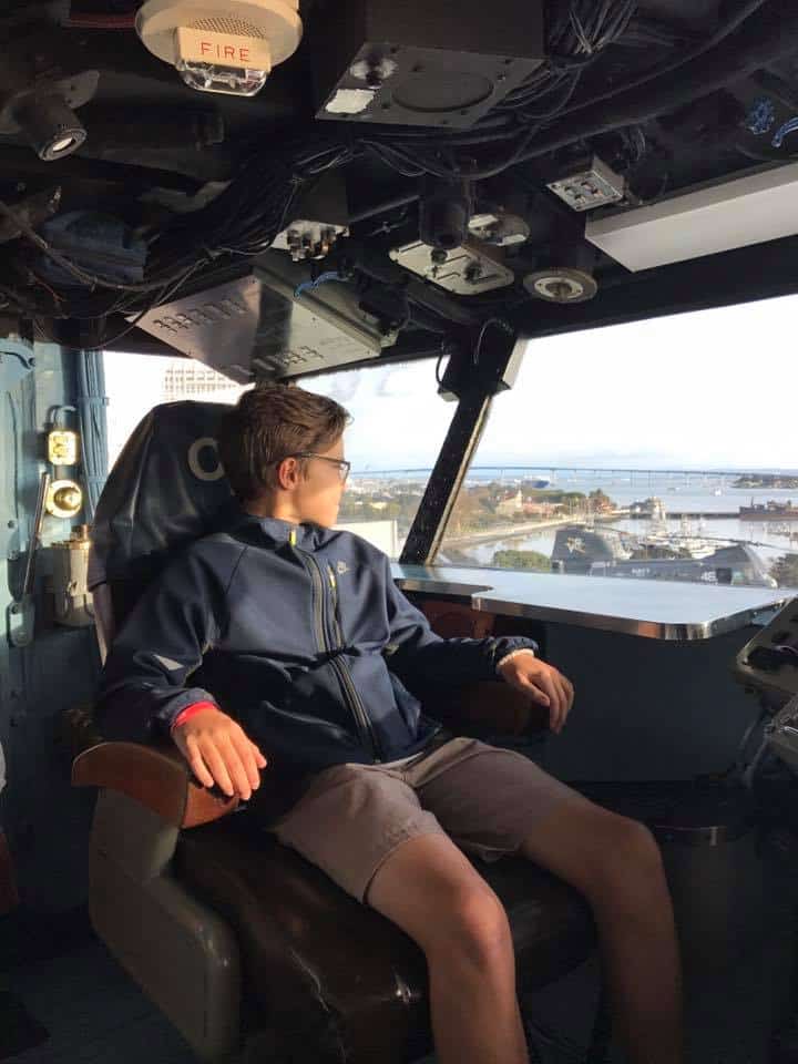 Boy seated in cockpit of aircraft carrier during tour of USS Midway