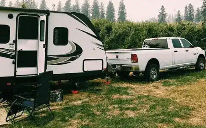 Travel trailer hitched to white truck and parked on private land.
