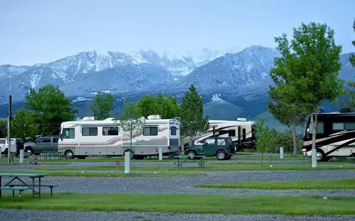 RVs and tow vehicles parked at a campsite with snow capped mountains in background