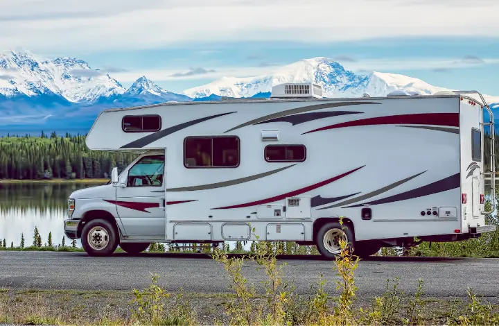 White motorhome RV driving near lake with snow-capped mountains in background