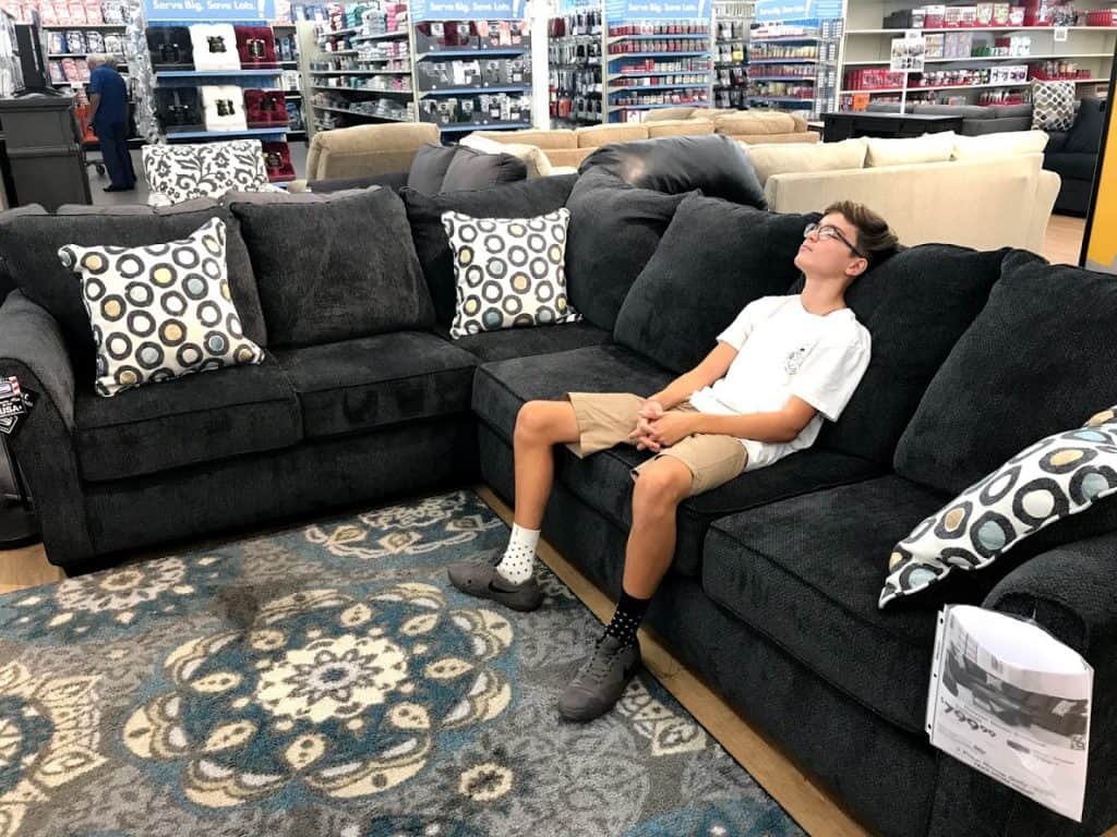 Boy resting on sofa as family looks for furniture for new apartment
