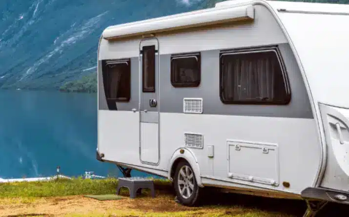 White travel trailer parked near lake with mountains in background.