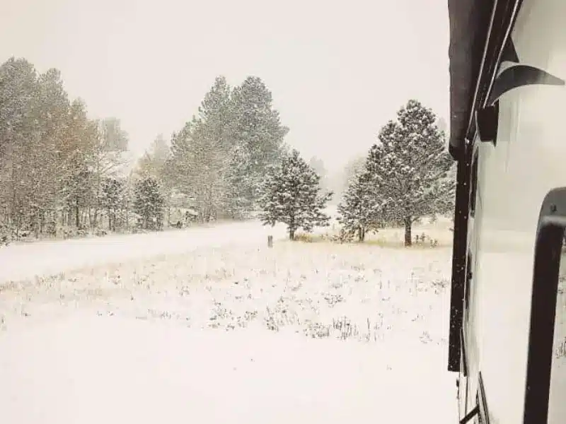 Side of RV and snow covered campsite.