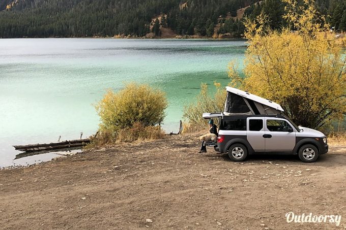 Grey truck camper with pop up tent parked at lake and available for rent near Yellowstone National Park