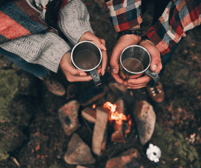 Two people holding coffee mugs over campfire