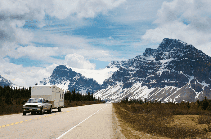 Truck and Travel Trailer driven on road with snow capped mountains in background