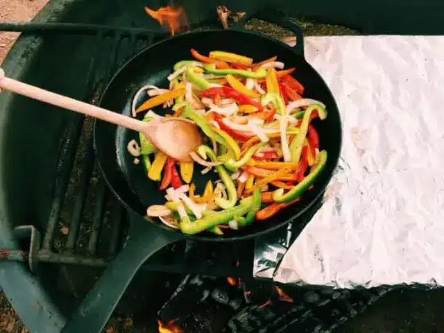 Fajita vegetables cooking in cast iron pan over campfire