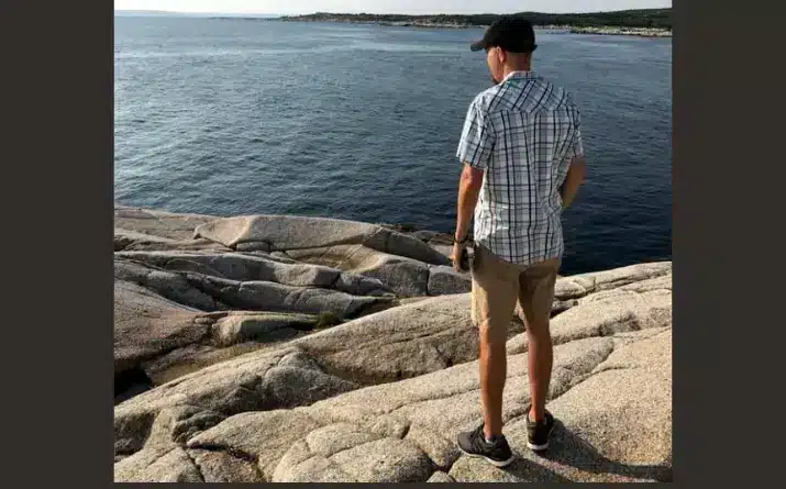 Man standing alone on rock looking out at ocean.