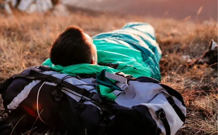 Man inside a sleeping bag with head on backpack.