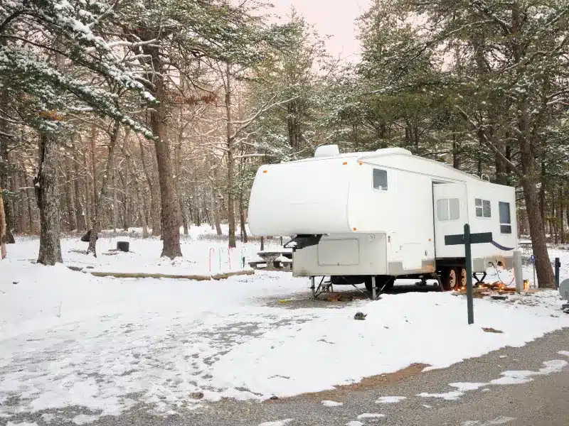 A white fifth wheel trailer parked at campsite during winter.