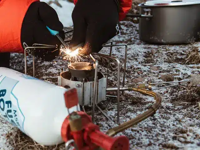 Camper wearing black gloves ignites a small outdoor stove with spark.