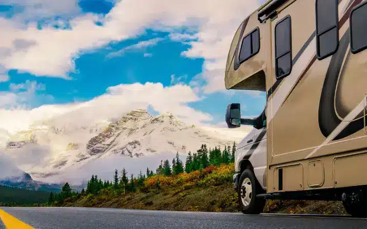 Class C RV on road driving toward snow-capped mountains