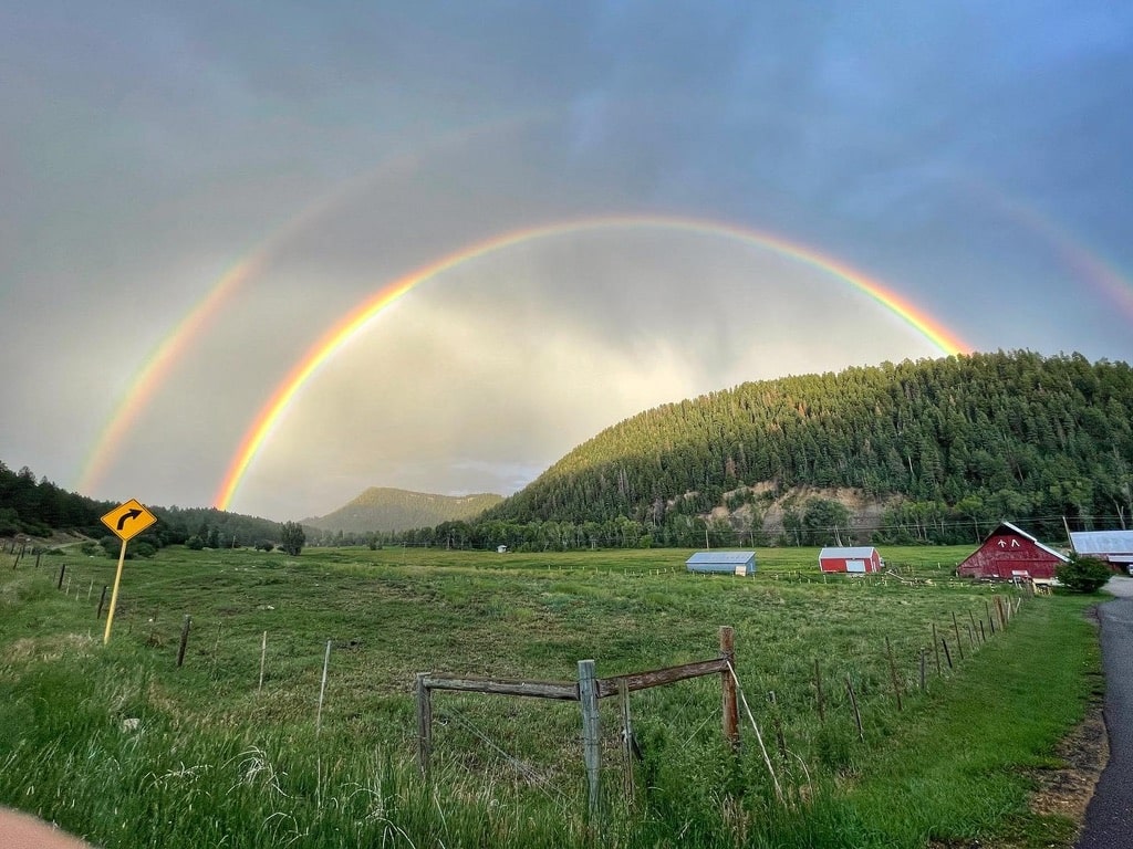 Full double rainbow visible above farm pasture in Durango Colorado