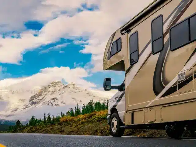 RV on open road with snow capped mountains in background