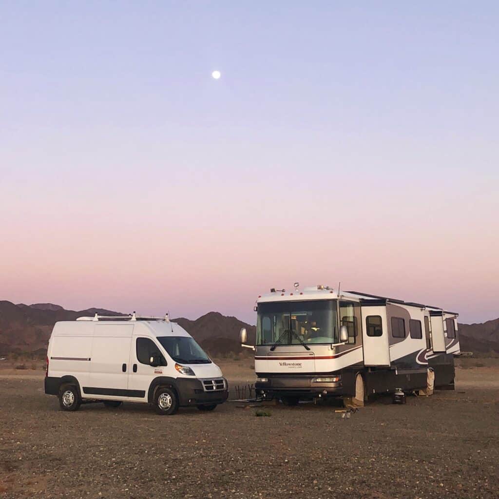 Camper van and large motor home parked in desert under moon