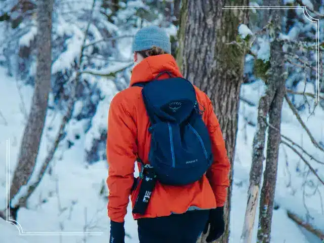 Man wearing red winter jacket and day hiking backpack during hike on snow covered trail