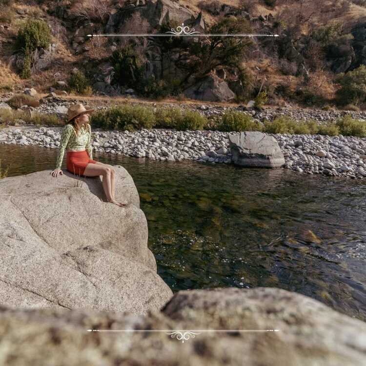 Woman sitting on large boulder near river