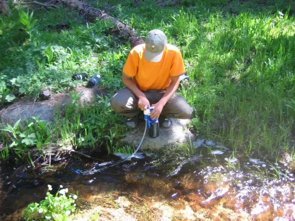 Hiker filtering water from stream for drinking.