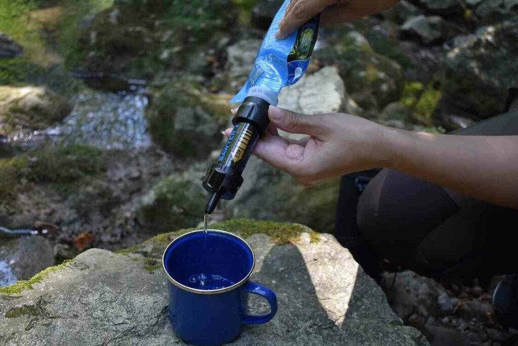 Hiker filtering water from stream into cup.