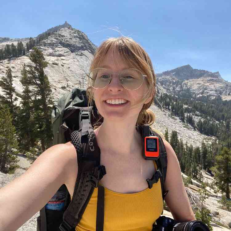 Woman in yellow tank top carrying large backpack while on a solo hiking trip.