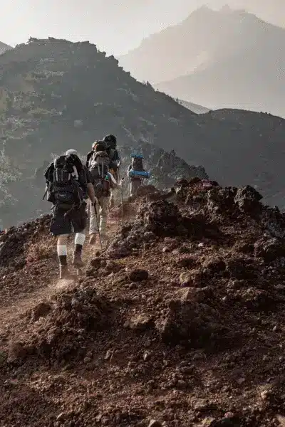 Three hikers with backpacks on trail near top of mountain range.