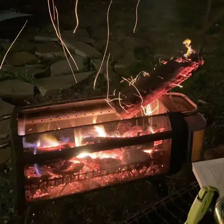 A burning log being turned and placed into portable fire pit at campsite