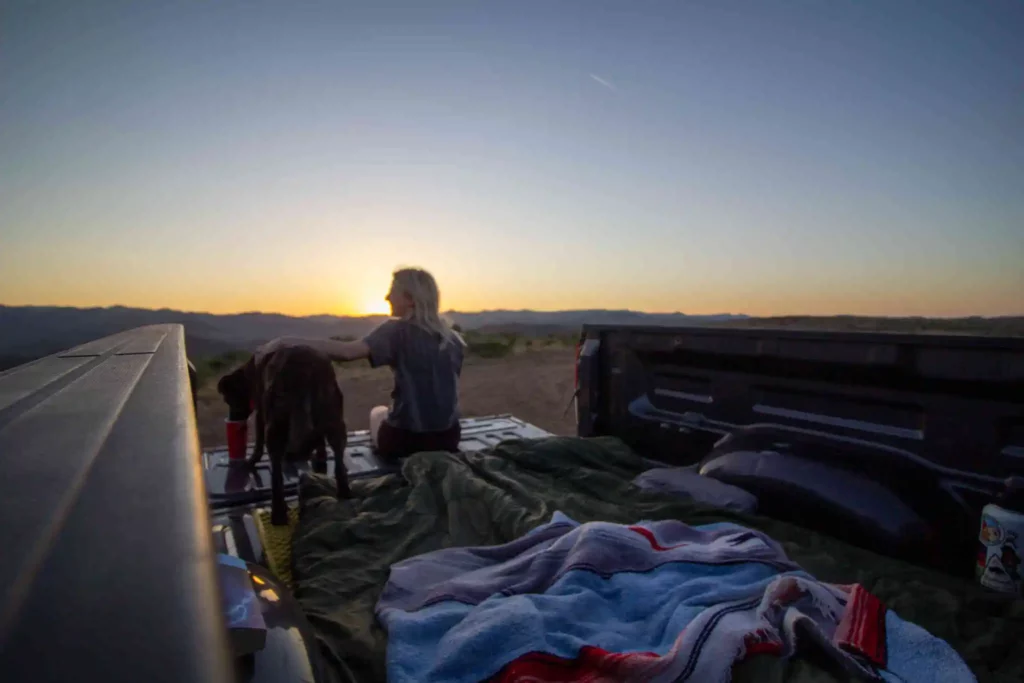 Girl and dog sitting in the back bed of a truck during camping trip.