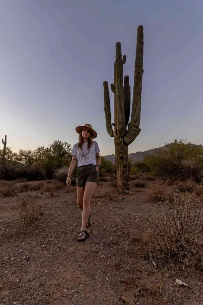 Woman wearing hat and shorts walking in front of cactus