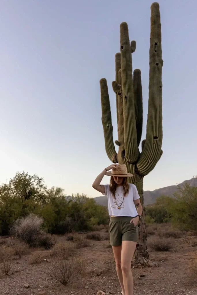 Woman wearing hat and shorts looking down in front of cactus