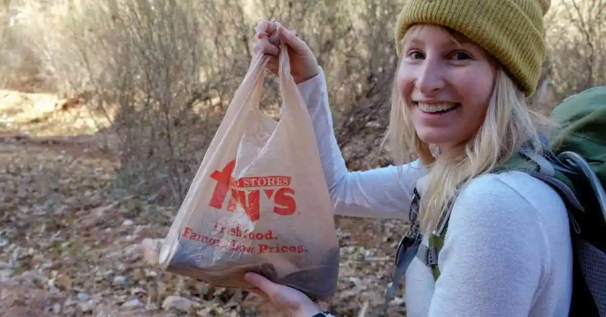 Woman hiker holds up a bag of trash picked up on trail as evidence for why principles of Leave No Trace are important