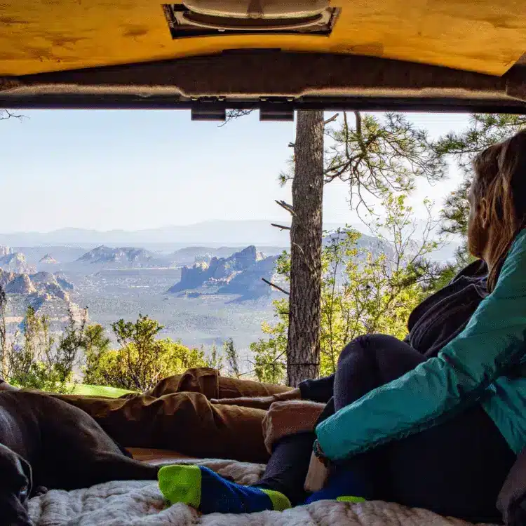 Man and woman inside campervan enjoying the view of mountains and forest through back window