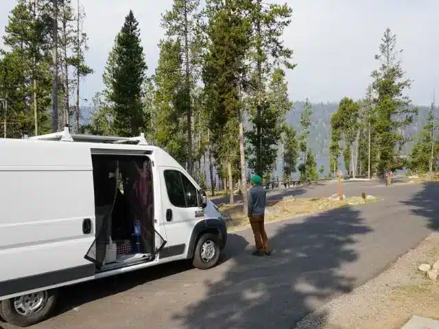 Man standing next to white campervan near the campsite.