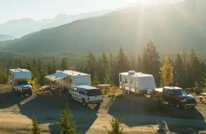 Group of RVs, travel trailers and trucks parked together with mountains in background.