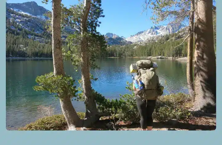 Experienced hiker carrying backpack views the lake while hiking Sierra Mountains