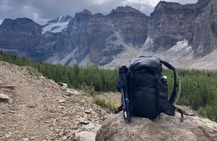Black REI backpack set on rock next to hiking trail with mountain range in background