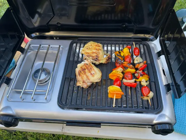 Chicken and veggie skewers cooking on outdoor grill.