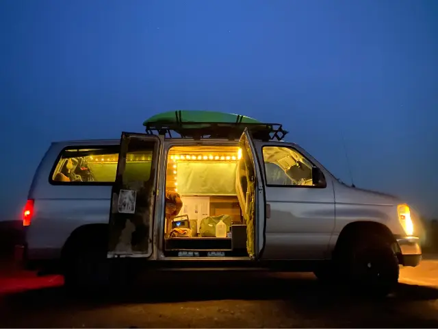Campervan with interior lots on and doors open, parked at night.