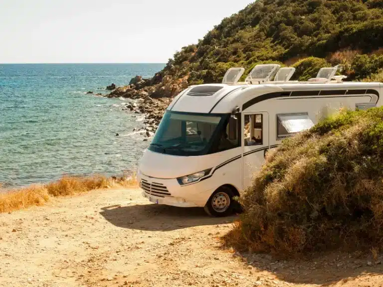 White Class B+ RV parked near ocean.